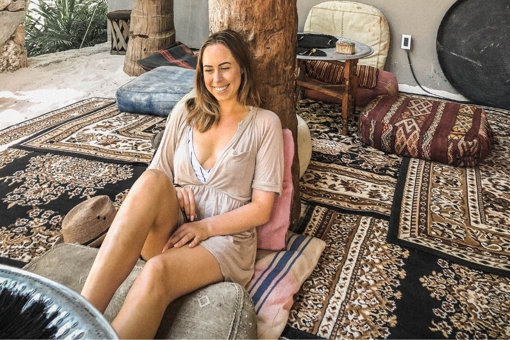 Woman lounging in a La Valeta public space in Tulum with rugs on the ground and fashionable beach garb. 