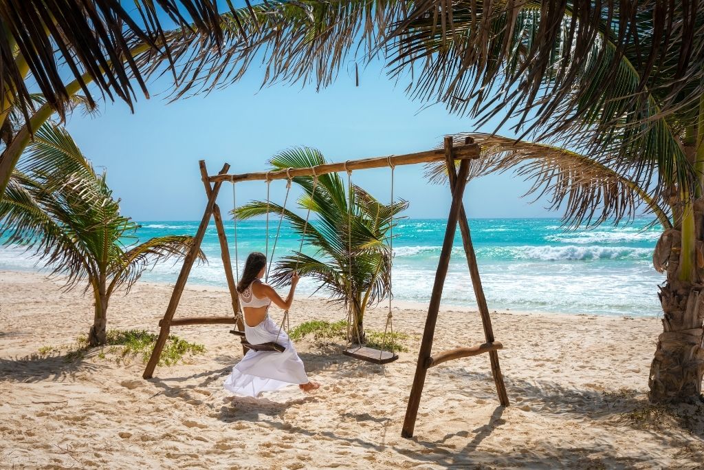 Woman swinging on a swing on the beach in Tulum's hotel zone.